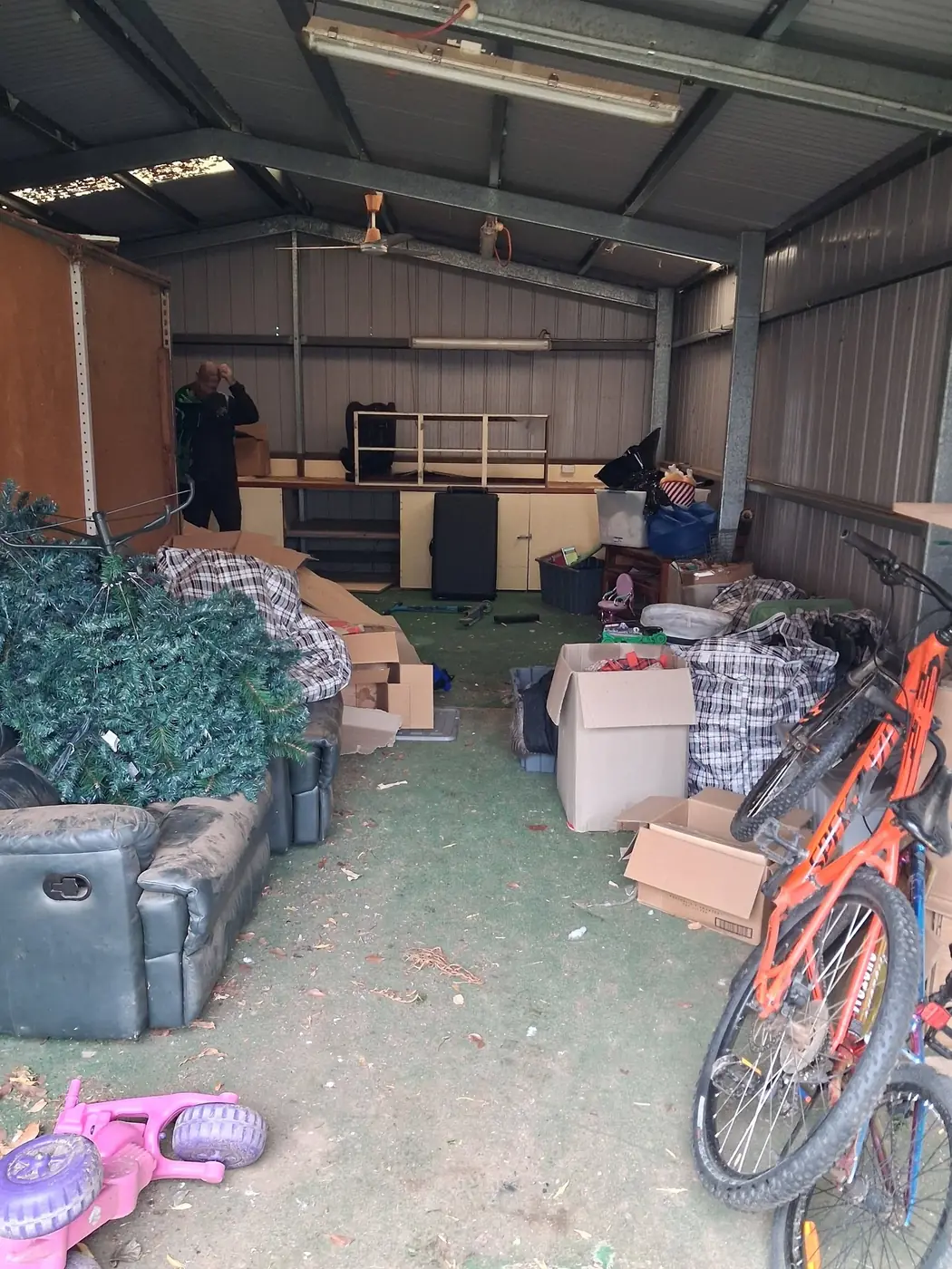 A backyard shed crammed with furniture, boxes, a bike and children's toys