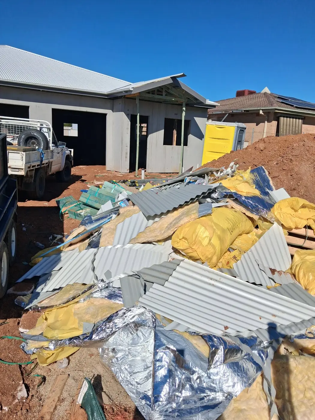 A large pile of old corrugated roofing sheets and packaging dumped outside a house under construction