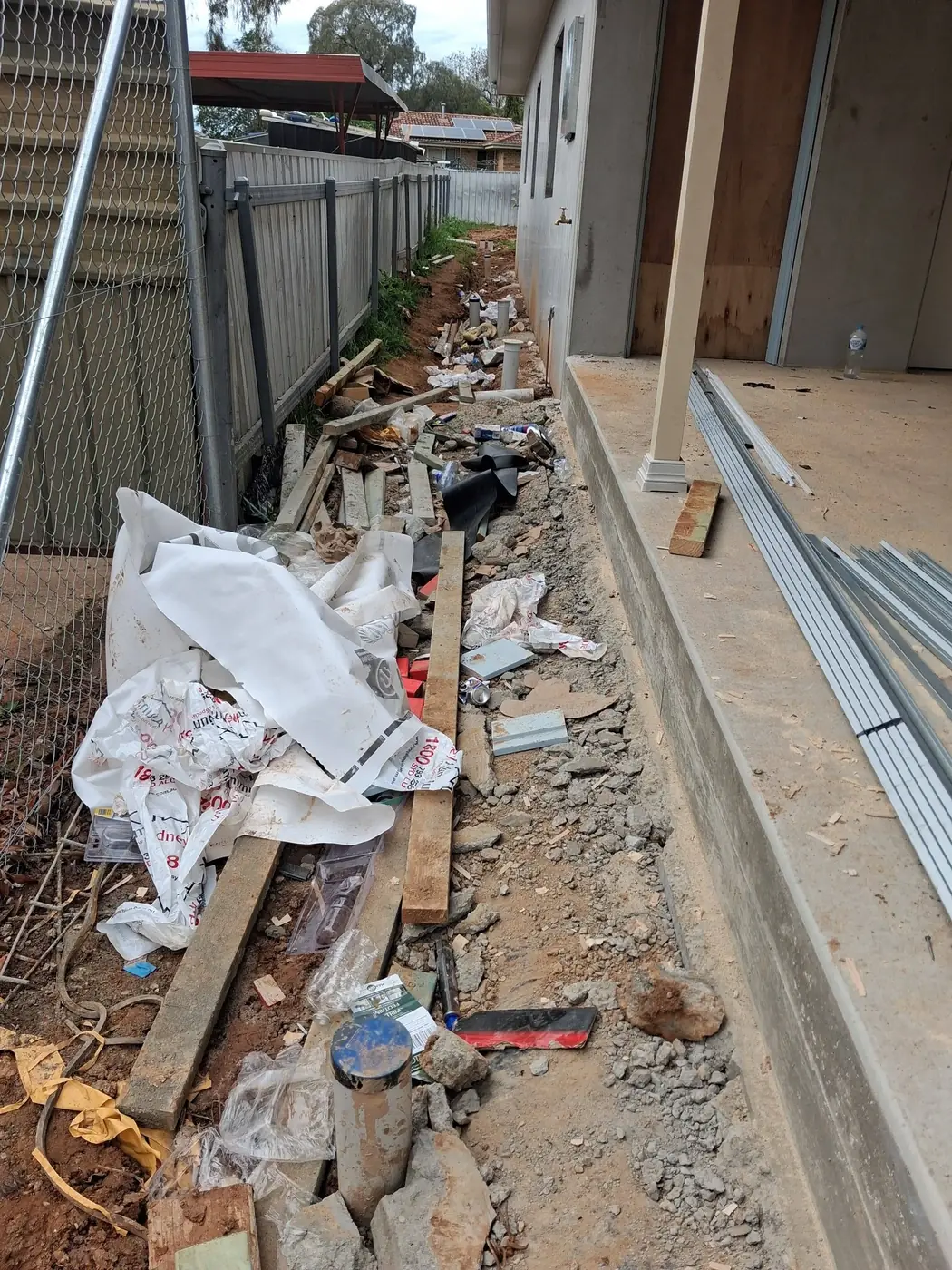 A narrow alley beside a house under construction, full of offcuts, packaging and building debris