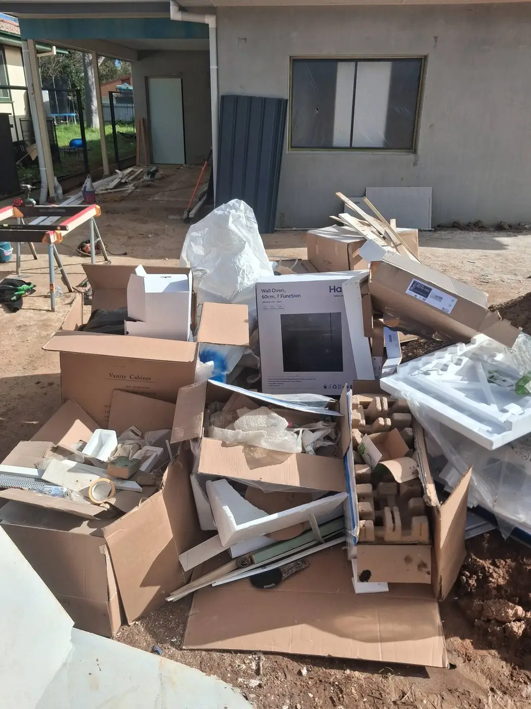 A renovation site with a pile of cardboard and demolition debris stacked against the house