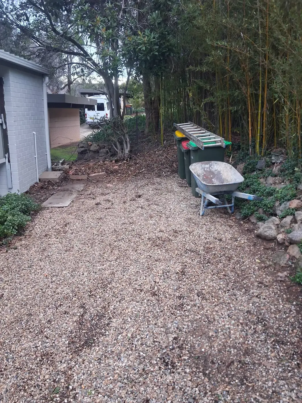 The same gravel path cleared, with only a wheelbarrow and bin left