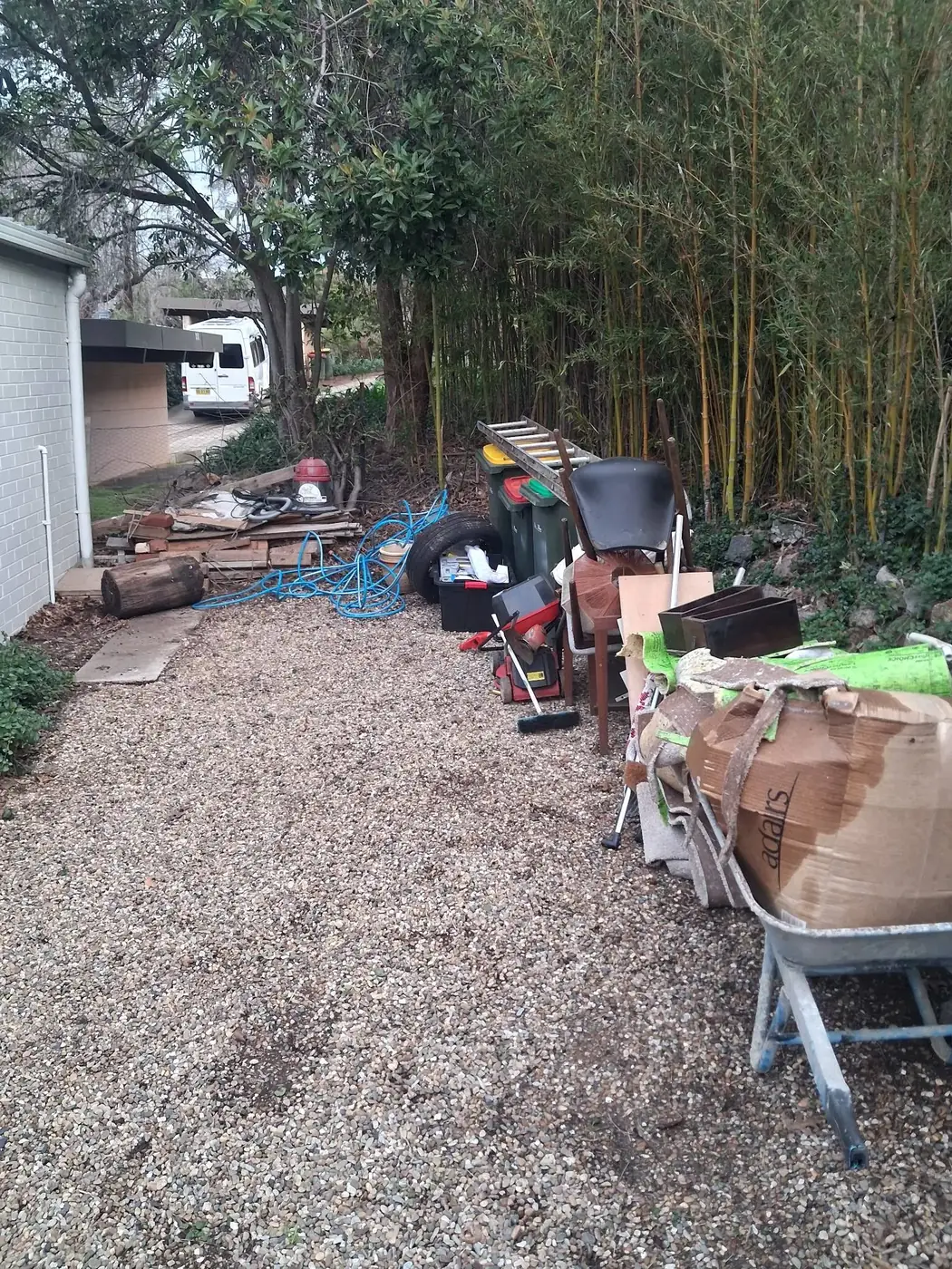 A gravel path stacked with yard waste, tools and bagged debris