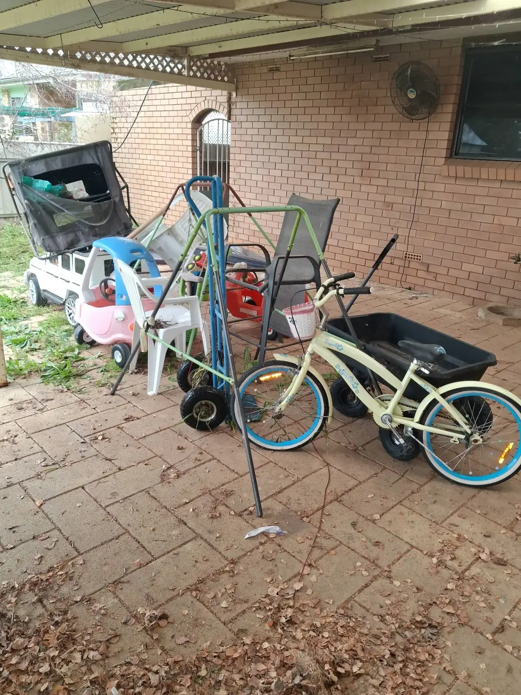 A brick-paved courtyard cluttered with bikes, chairs, a wagon and assorted junk