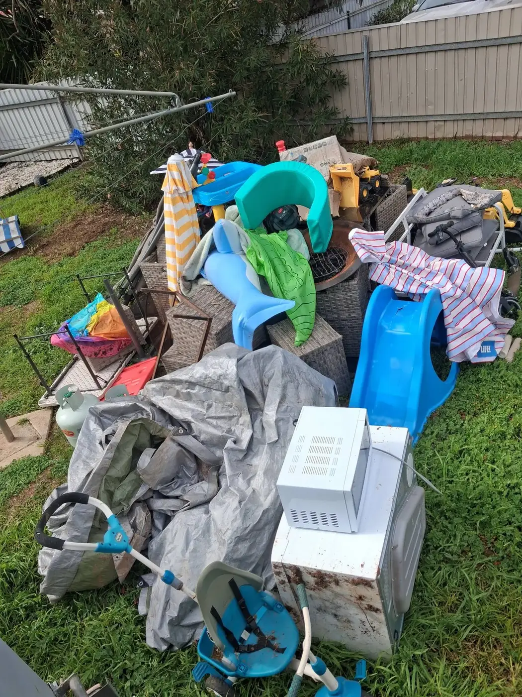 A backyard with a pile of children's toys and household items dumped on the grass