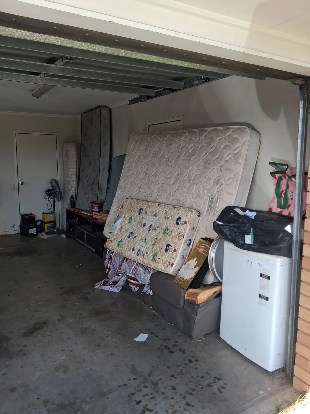 A garage with a mattress, TV unit and washing machine piled against the wall