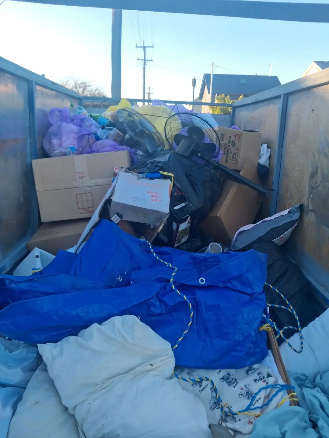 A trailer loaded with a household clear-out: boxes, a mattress and a strapped tarp