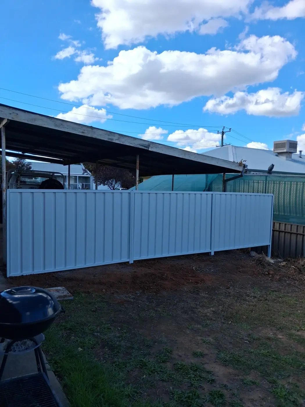 A newly installed cream colourbond fence running alongside a carport