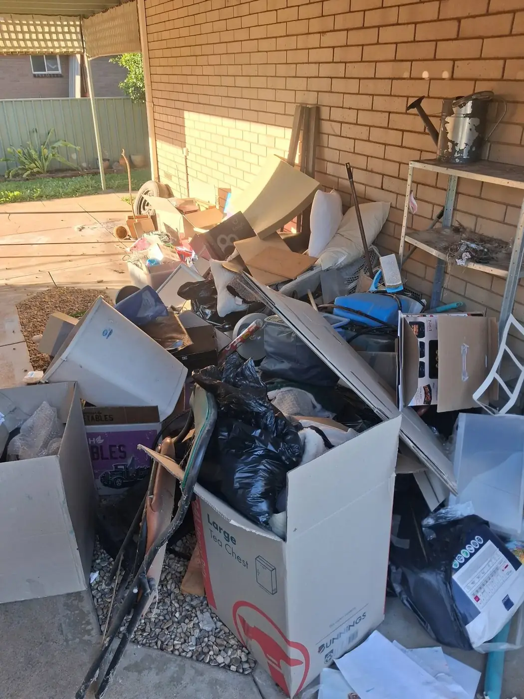 A patio stacked with boxes and household junk against a brick house before a clean-out